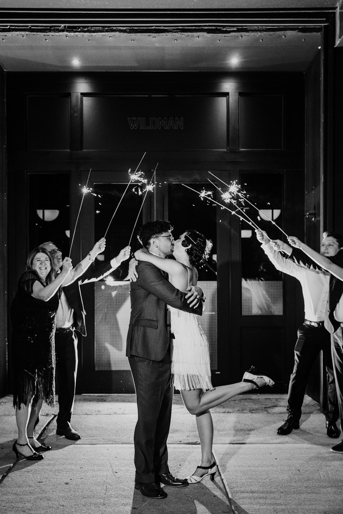 A couple kisses while guests hold sparklers around them outside at night, celebrating joyfully at their Wildman BT wedding.