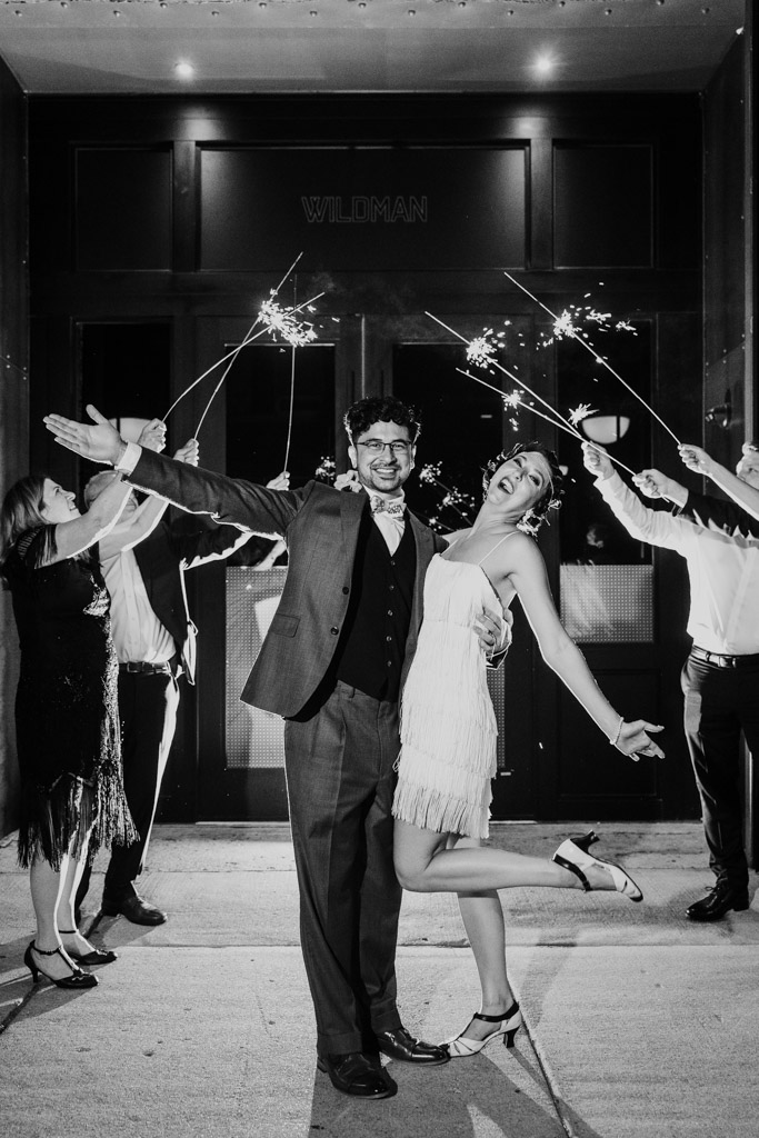 A joyous couple poses outside at night during their Wildman BT wedding, surrounded by friends holding sparklers.