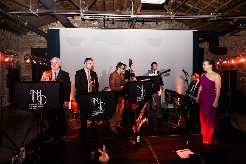 A jazz band performs on stage in formal attire, with a female vocalist in a magenta dress at the right, creating an elegant atmosphere perfect for a Wildman BT wedding.