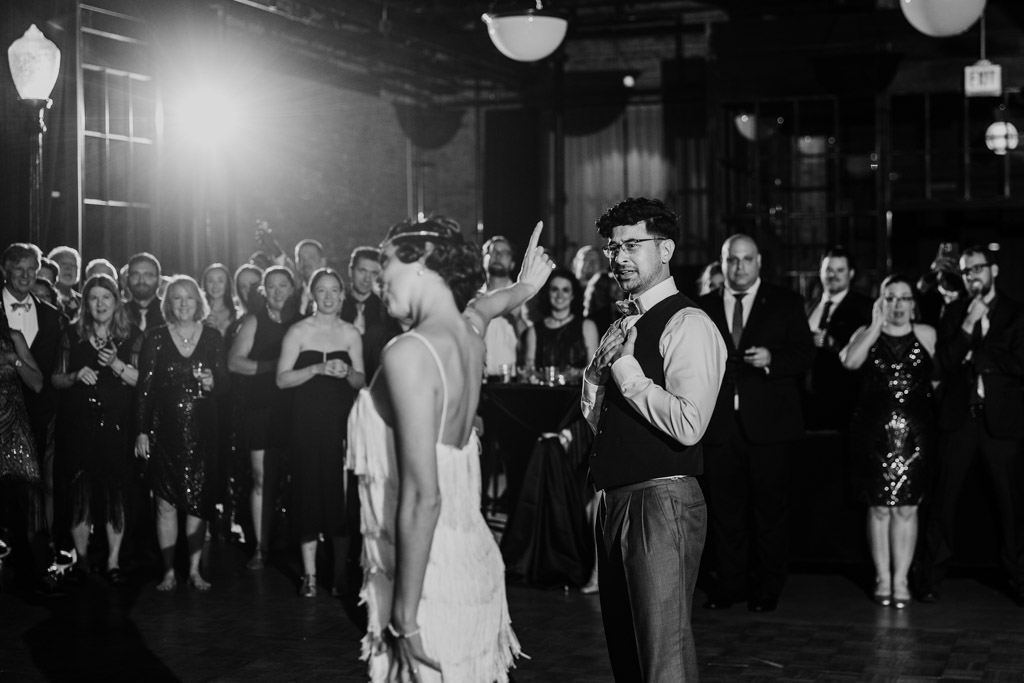 At a Wildman BT wedding, a woman dances and gestures to a man in front of a crowd at the formal event, everyone smiling.