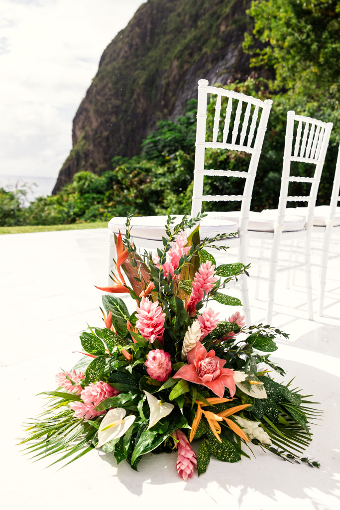 Tropical flower arrangement beside white chairs outdoors at Viceroy Sugar Beach, with a mountain and lush greenery in the background