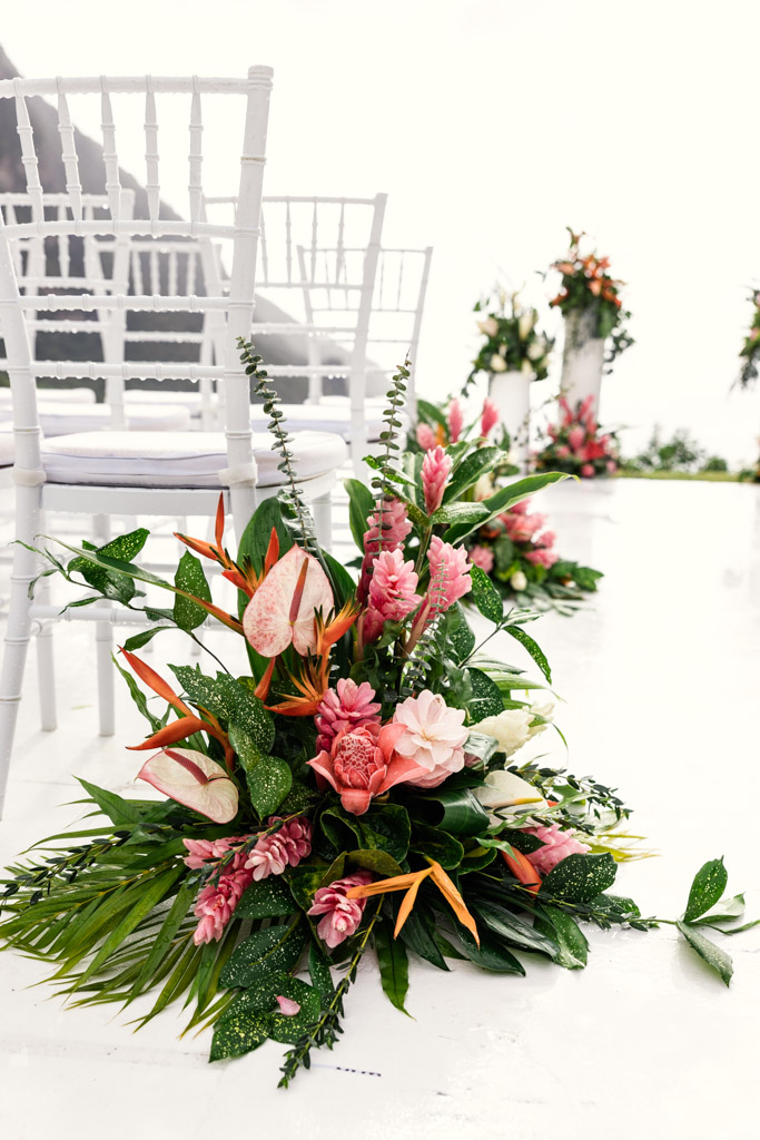 Tropical flower arrangement with pink and orange blooms beside white chairs at an outdoor Viceroy Sugar Beach wedding ceremony