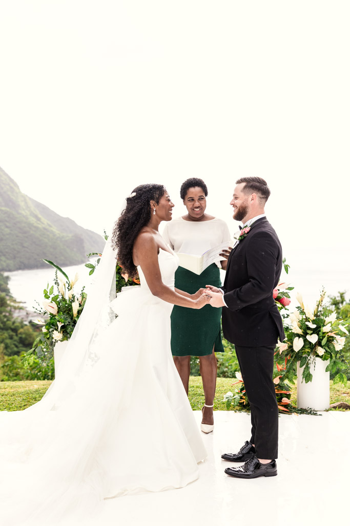 Bride and groom holding hands during an outdoor wedding ceremony at Viceroy Sugar Beach, with officiant and lush floral arrangements behind them