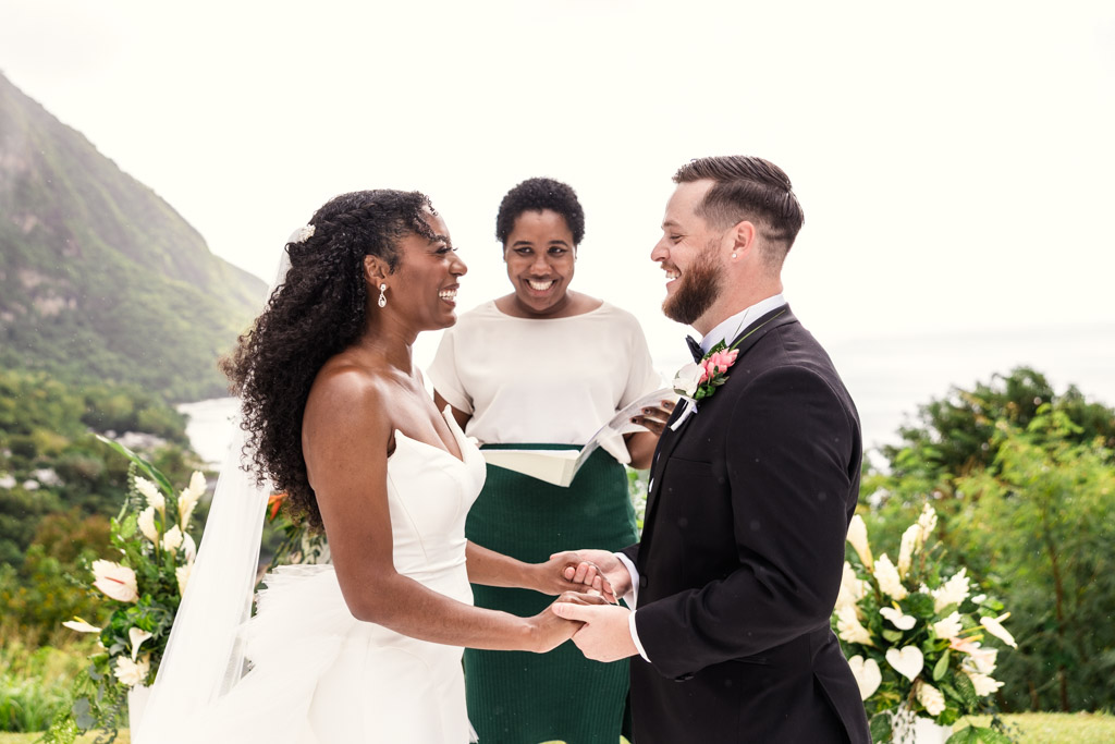 Bride and groom smiling and holding hands during an outdoor wedding ceremony at Viceroy Sugar Beach, officiant standing behind them