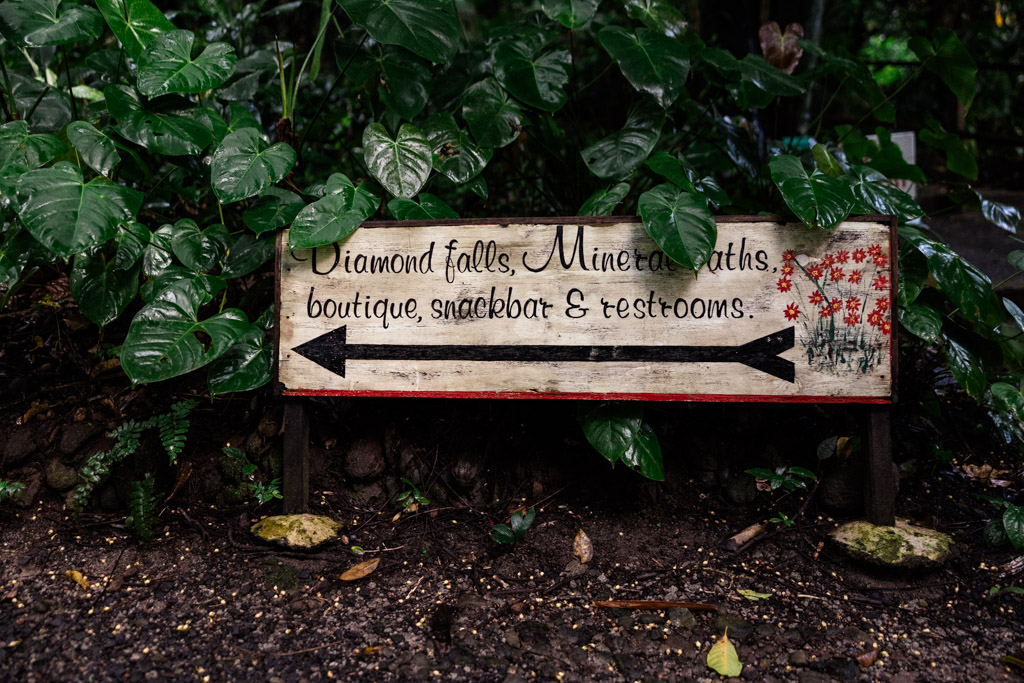 Wooden sign in lush greenery points to Diamond Falls, mineral baths, boutique, snack bar, restrooms