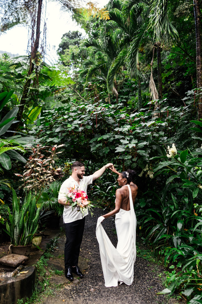 Bride and groom dance on a lush garden path at Diamond Falls Botanical Gardens, with the groom holding a bouquet and the bride in a white dress