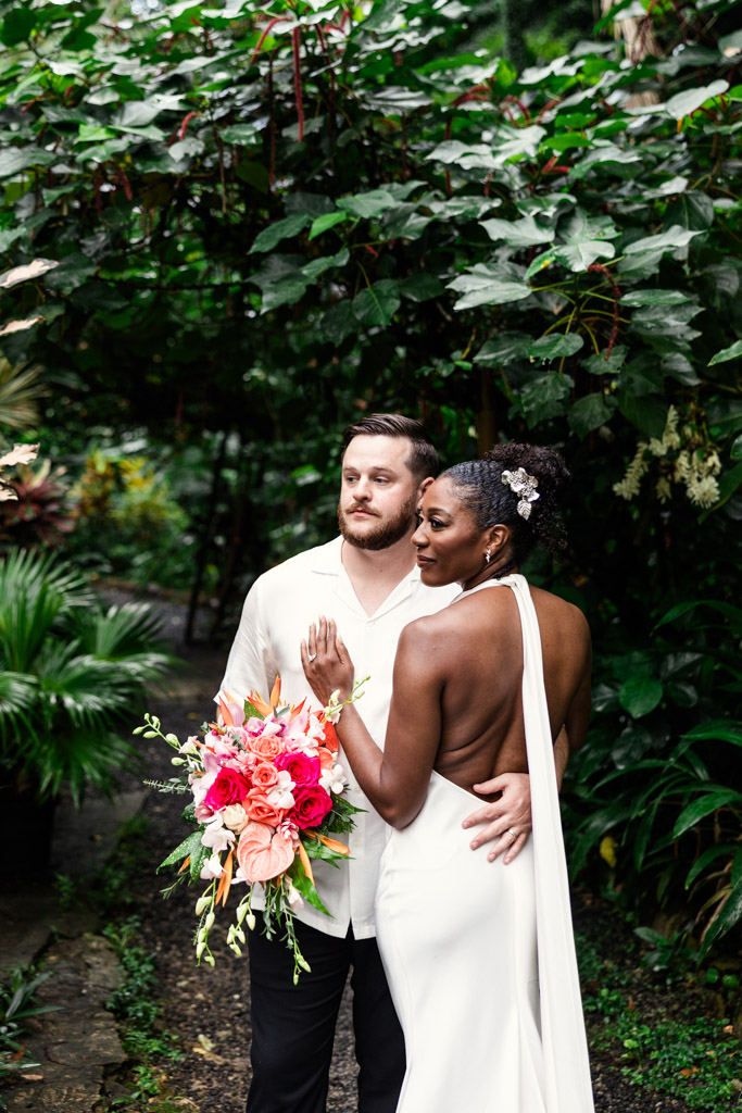 Bride in a white dress and groom in white shirt pose together in the lush Diamond Falls Botanical Gardens