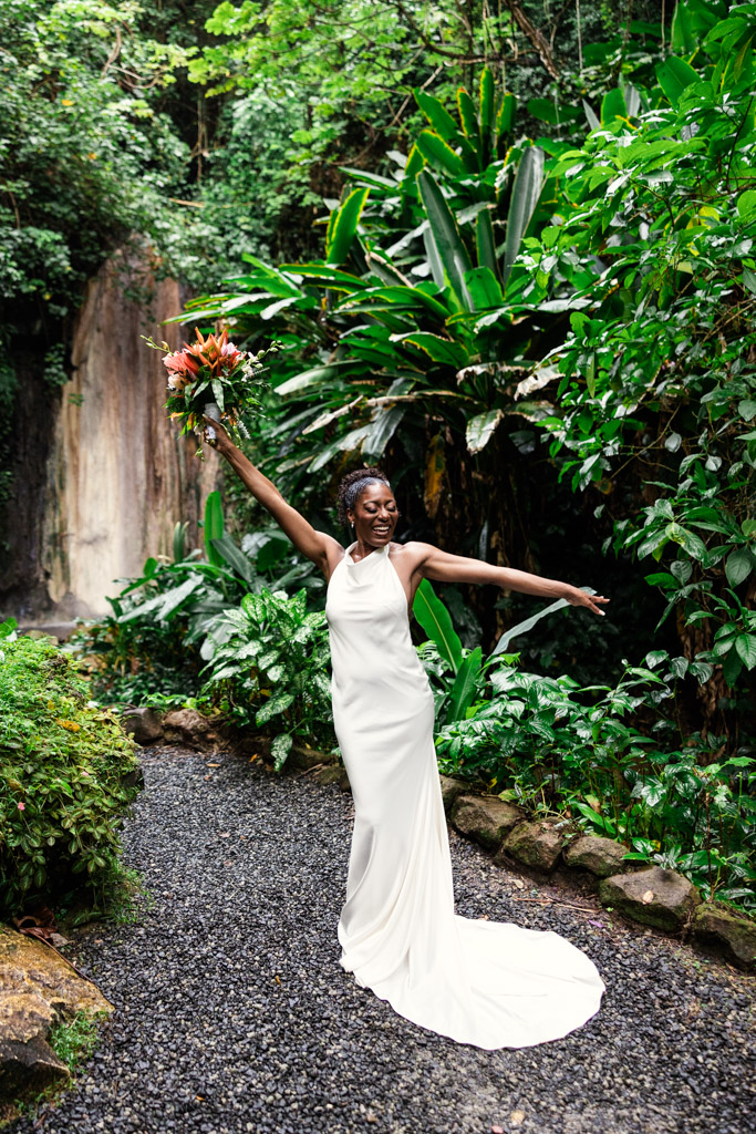 Happy bride in a white dress poses with a bouquet in the lush, tropical garden setting of Diamond Falls Botanical Gardens