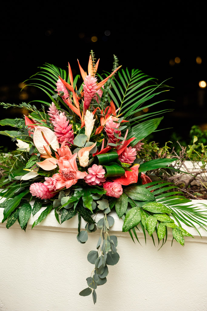 Pink and orange tropical flower arrangement with lush green leaves sits on a white ledge for wedding celebration at Viceroy Sugar Beach