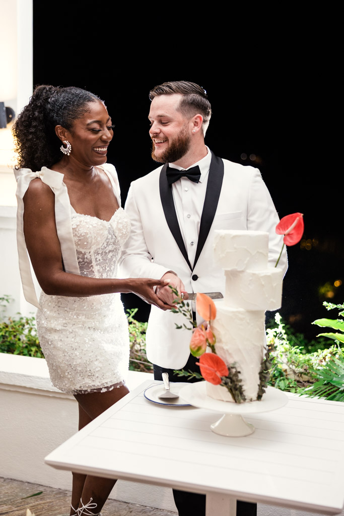 Happy bride and groom in formal attire slices their wedding cake together at night at Viceroy Sugar Beach