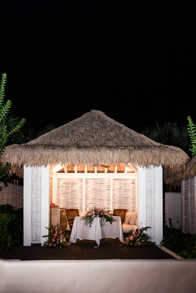 A thatched-roof gazebo at night, decorated with flowers and a table set for two at Viceroy Sugar Beach
