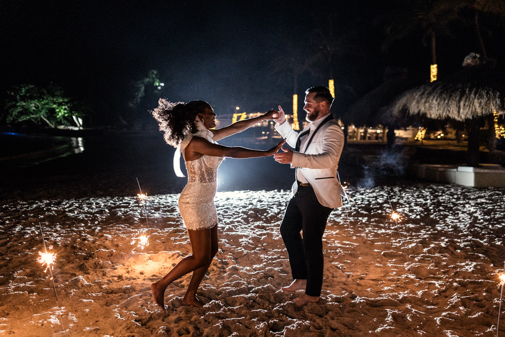 Couple dances joyfully on the sandy shores of Viceroy Sugar Beach at night, surrounded by sparklers and festive lights