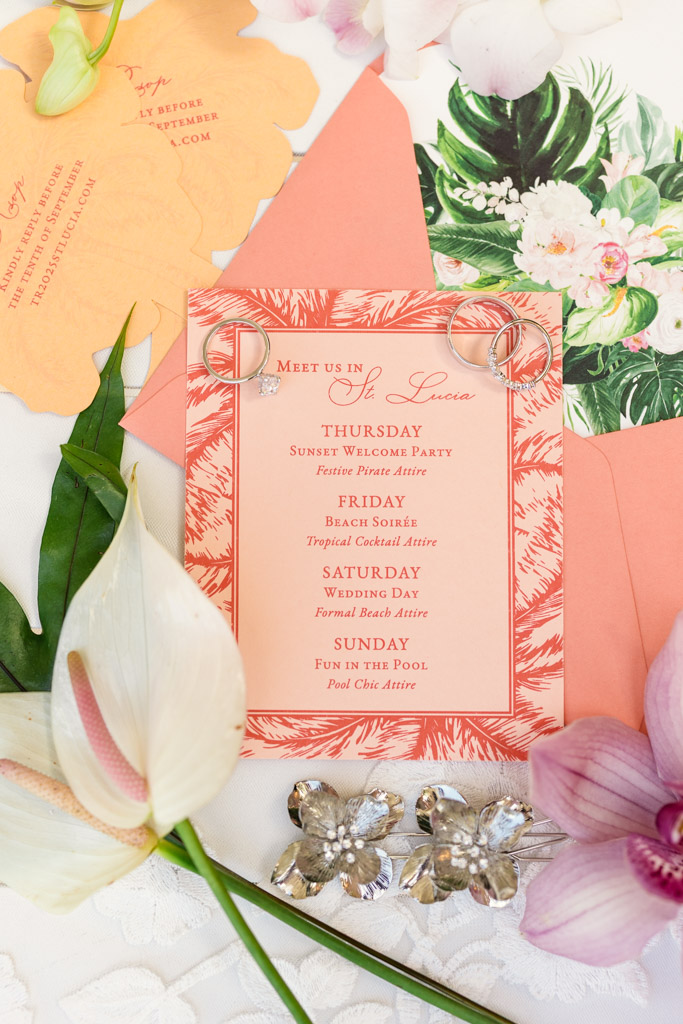 Coral and peach wedding invitation with rings, flowers, and leaves arranged decoratively around it for a Viceroy Sugar Beach wedding celebration