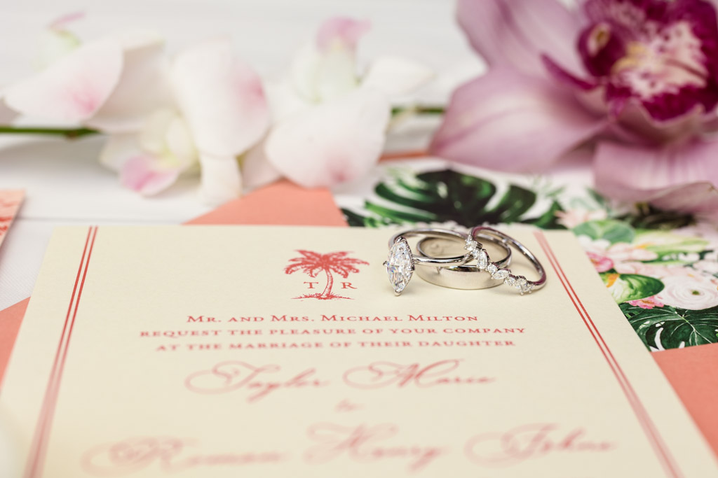 Wedding invitation with two rings on top, surrounded by pink flowers and floral decorations for Viceroy Sugar Beach wedding celebration