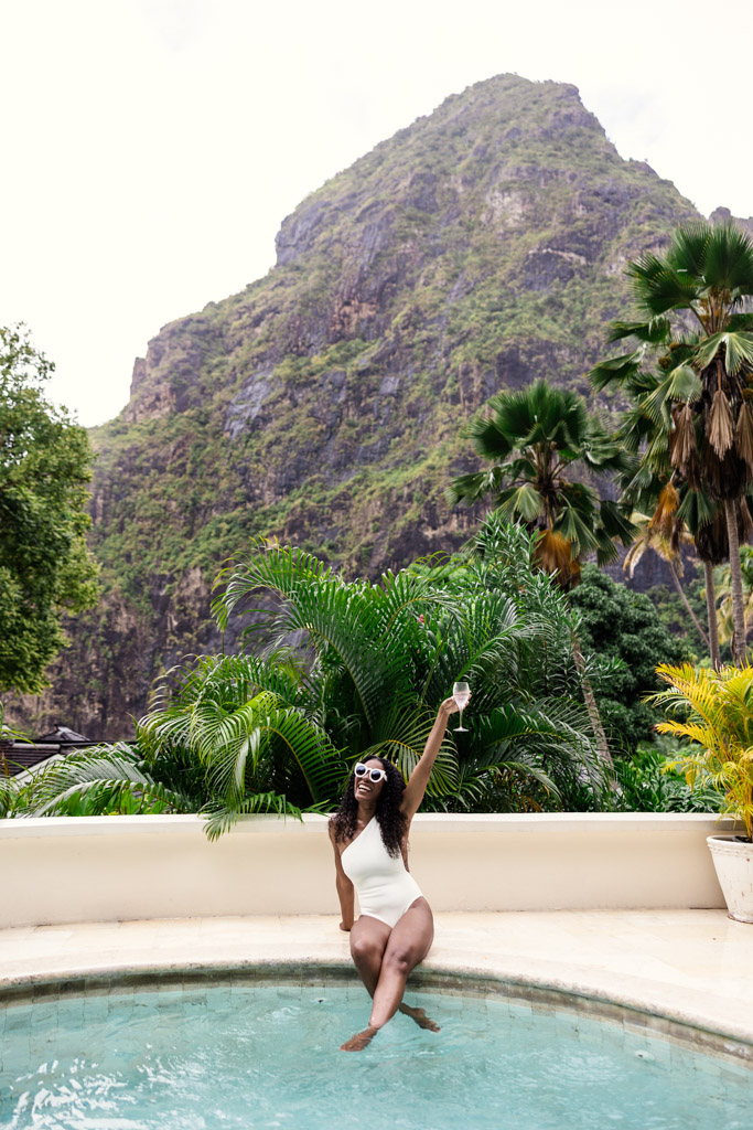 Bride in a white swimsuit holds a glass of champagne by the pool at her room at Viceroy Sugar Beach with Petit Piton in the background