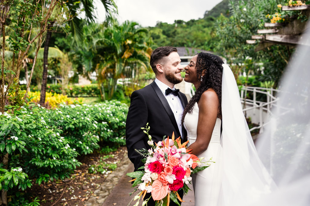 Bride and groom smiling at each other in a lush garden at Viceroy Sugar Beach, bride holding a bright bouquet.