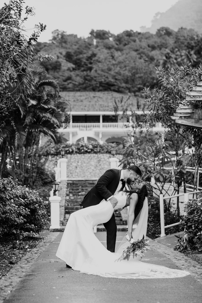 Black and white photo of groom dipping and kissing his bride outdoors on the grounds of Viceroy Sugar Beach, surrounded by lush greenery