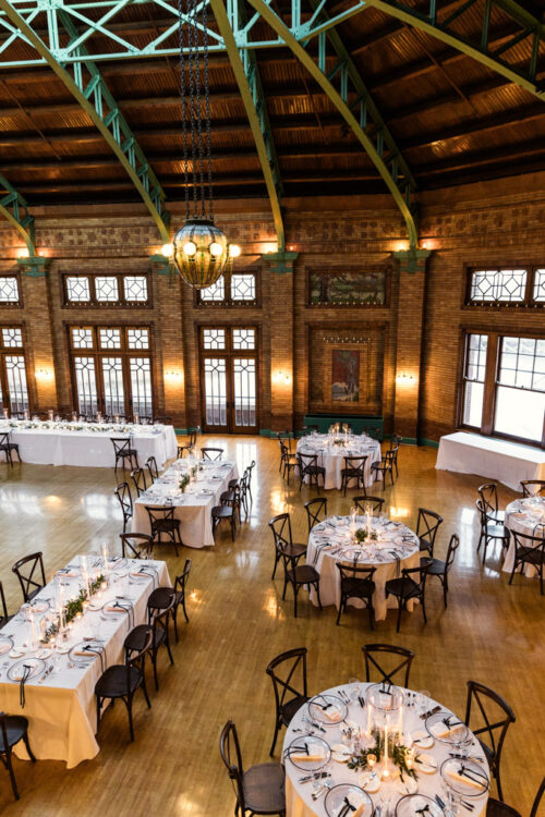 Elegant banquet hall with round tables set for an event, under a high wooden ceiling and large windows.