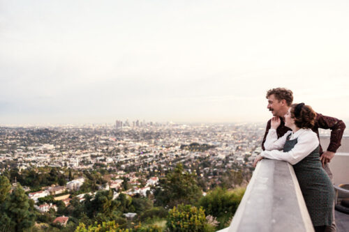 Engaged couple looks at the Los angeles skyline from Griffith Park Observatory during spring engagement session