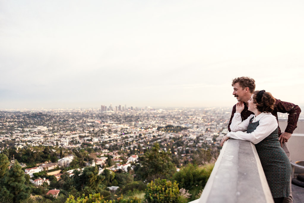 Engaged couple looks at the Los angeles skyline from Griffith Park Observatory during spring engagement session