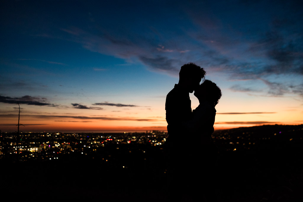 Silhouette of engaged couple embracing at sunset with Los Angeles city lights visible in the distance