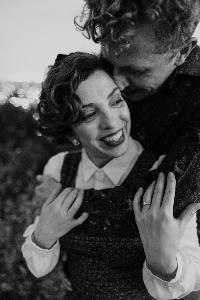 Black and white photo of couple embracing and smiling, the woman showing an engagement ring