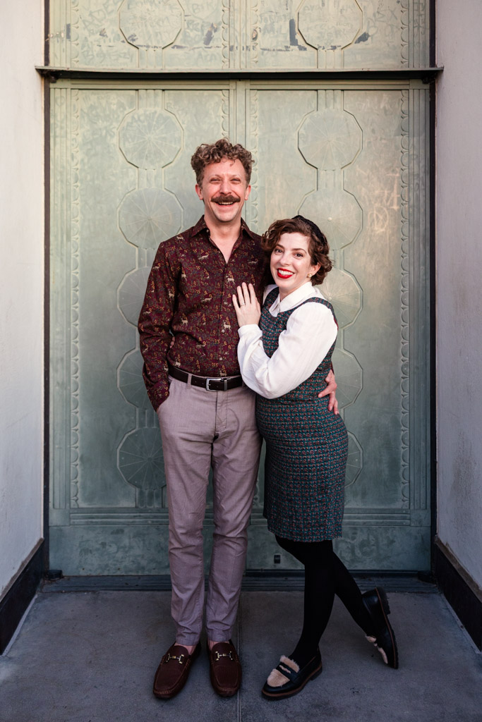 Happy engaged couple poses together in front of a tall, ornate green door at Griffith Park Observatory