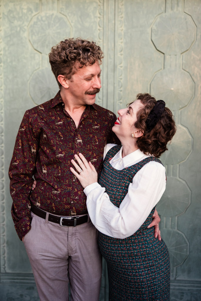 Candid photo of engaged couple smiling and looking at each other against a decorative green door at Griffith Park Observatory