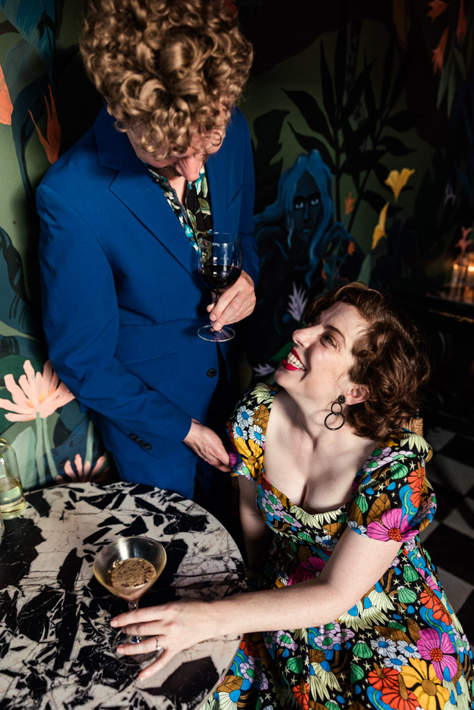 Two people in colorful outfits share a drink and smile at each other inside Justine's, a Los Angeles wine bar