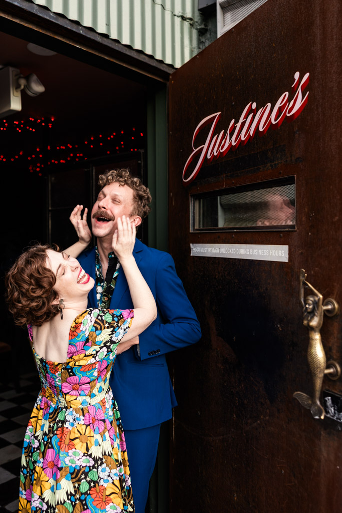 A smiling woman playfully grabs a laughing man's face in the doorway to Justine's, a Los Angeles wine bar