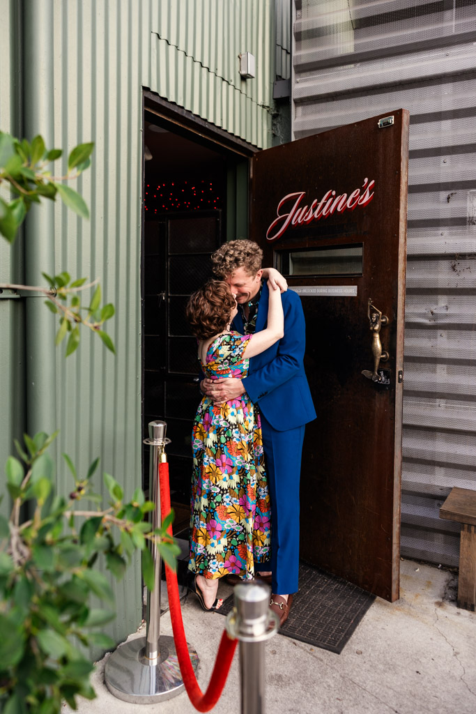Engaged couple embraces in the doorway of Justine’s wine bar