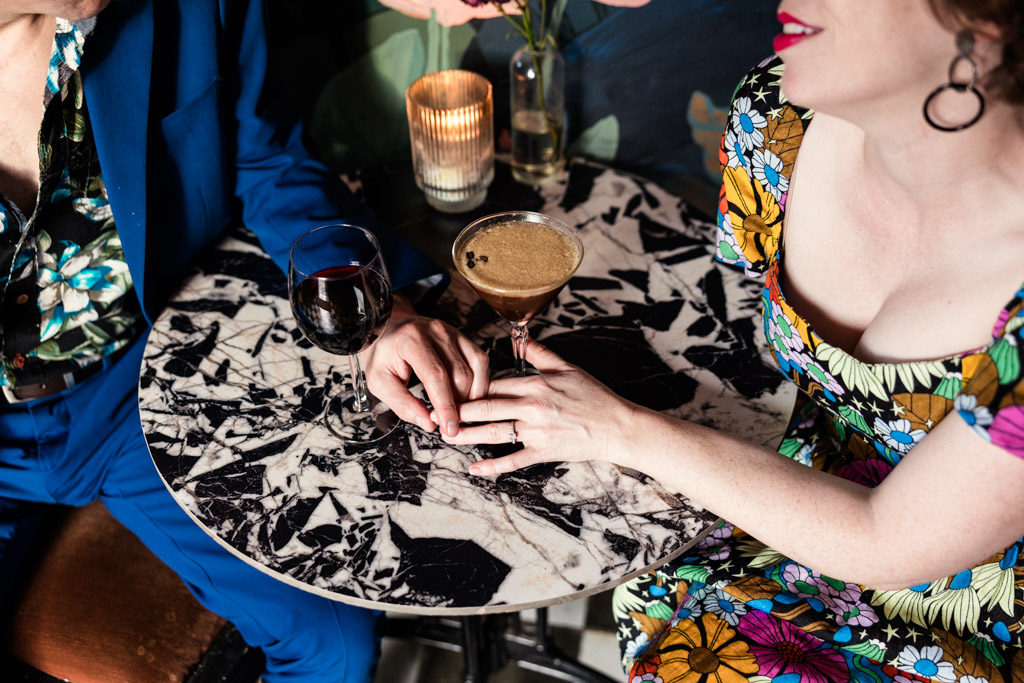 Engaged couple holding hands at a marble table with cocktails inside Justine's wine bar in Los Angeles