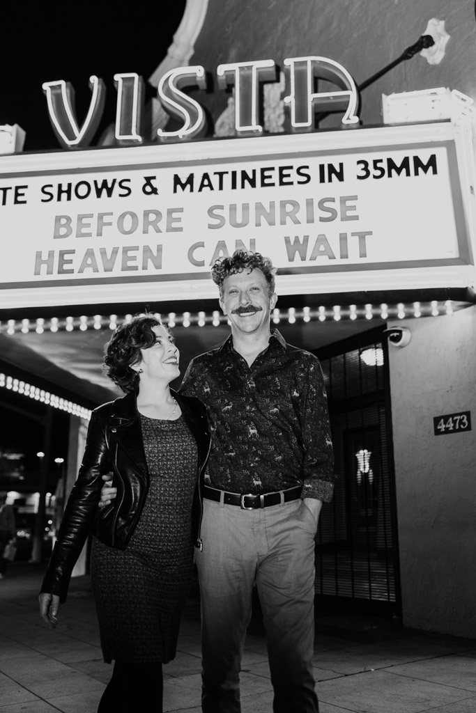 Black and white photo of smiling couple standing outside the Vista Theatre at night under the marquee
