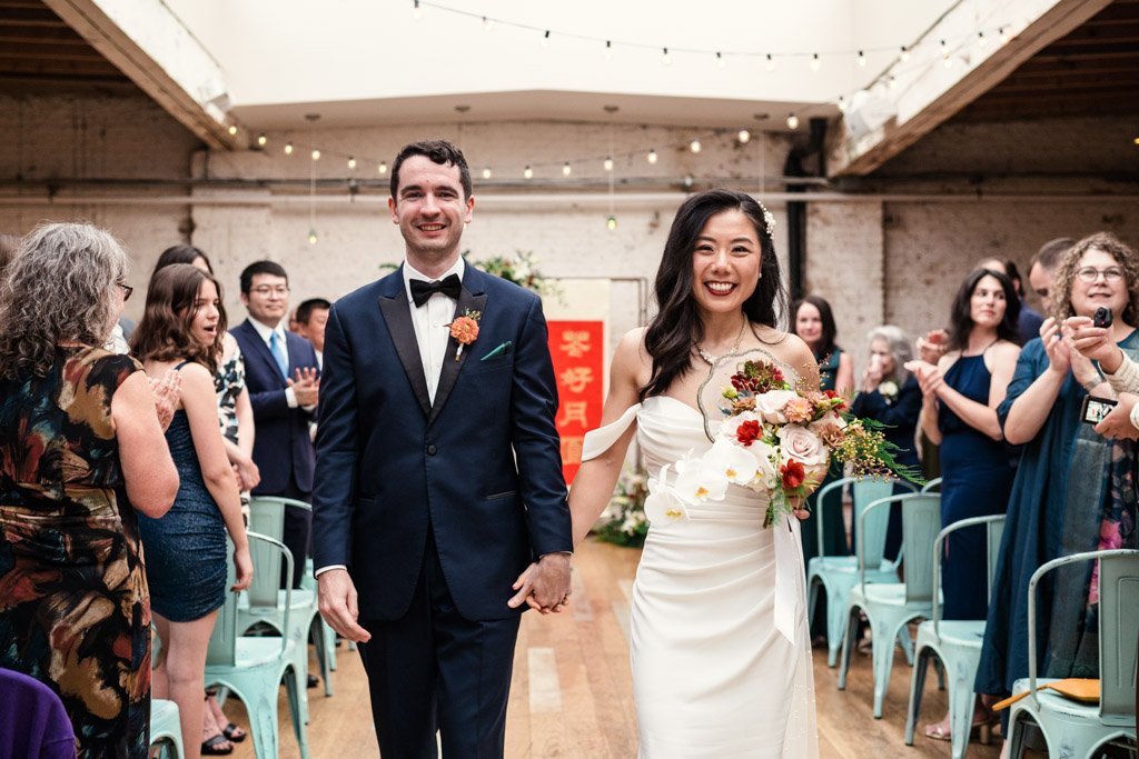 Happy bride and groom walk down the aisle while guests cheer after their Chicago wedding ceremony at The Joinery