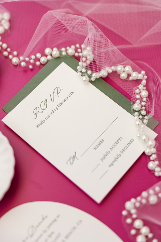 RSVP card with pearls and pink tulle on a bright pink background, partially revealing the Frente al Punto wedding details