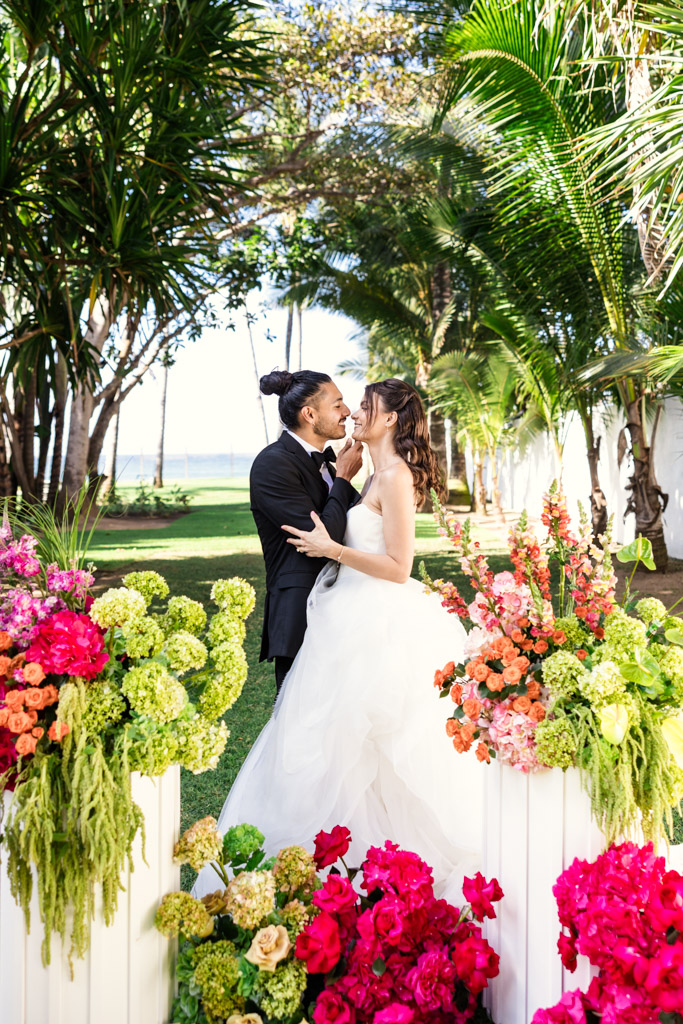 Bride and groom smiling and embracing outdoors at their Frente al Punto wedding, surrounded by vibrant flowers and lush greenery