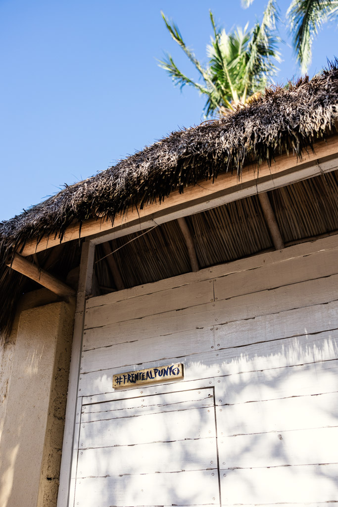 A white wooden hut with a thatched roof, palm leaves above at Frente al Punto wedding venue in Sayulita