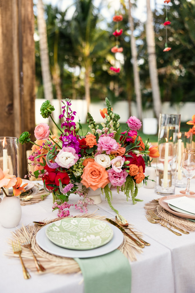 Colorful floral centerpiece on an elegant outdoor table set with candles, plates, and green napkins for a Frente al Punto wedding