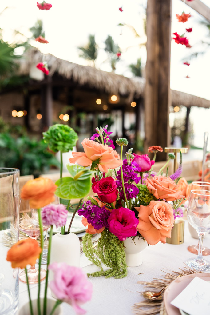 A vibrant floral centerpiece with pink, orange, and green flowers on an outdoor table setting for a Frente al Punto wedding