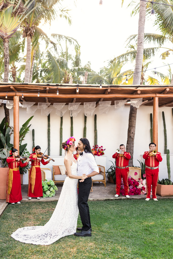 A bride and groom dance on grass as a mariachi band plays in the sunshine at a tropical Frente al Punto wedding
