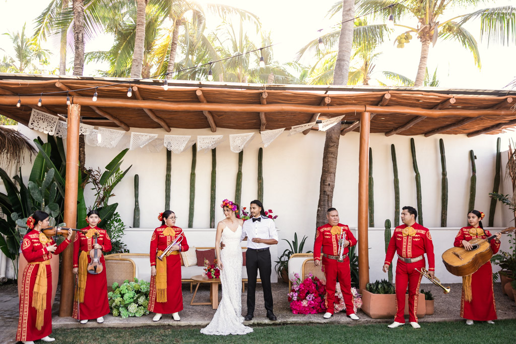 Bride and groom stand together outdoors at their Frente al Punto wedding, surrounded by a mariachi band dressed in vibrant red outfits