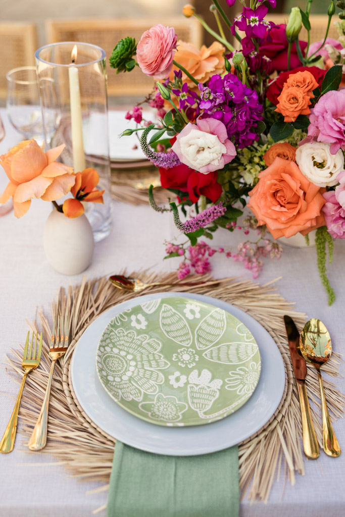 A floral table setting with a green patterned plate, gold cutlery, and a colorful bouquet centerpiece for an elegant Frente al Punto wedding celebration