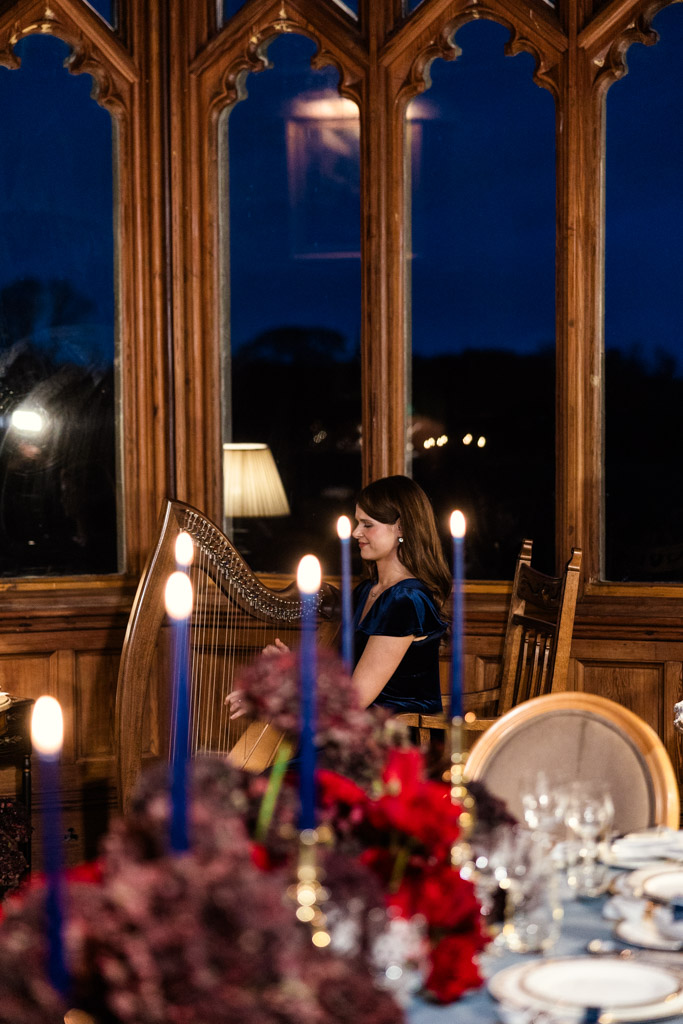 A woman plays the harp near tall windows in a candlelit room set for wedding dinner at Markree Castle