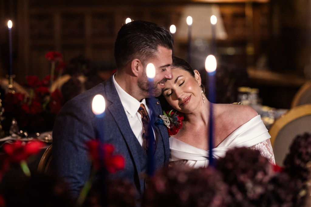 A couple sits closely and smiles, surrounded by candles and flowers at a dimly lit, elegant wedding celebration at Markree Castle