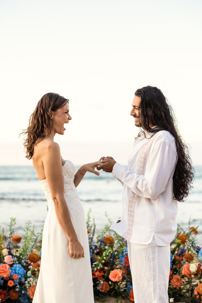Bride and groom exchange rings, smiling, during their Sayulita beach elopement with colorful flowers in the background