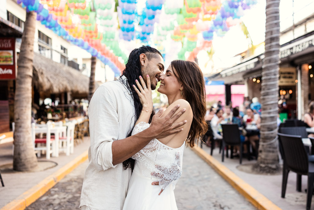 A couple shares a romantic kiss under colorful hanging decorations on a lively street in Sayulita