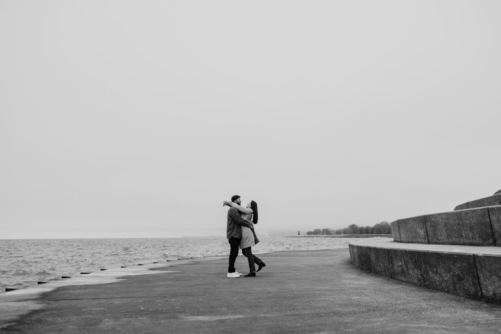 Black and white photo of couple hugging at Belmont Harbor on Chicago lakefront at sunrise