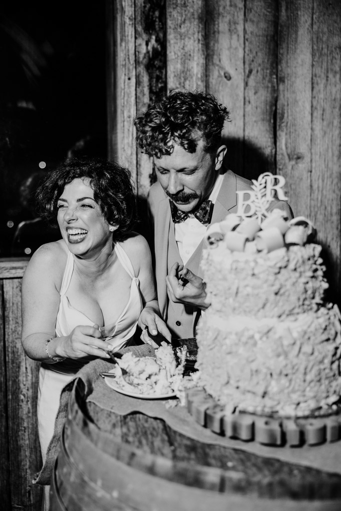 Happy newlywed couple laughs while eating their wedding cake together at Terra Mia Vineyard