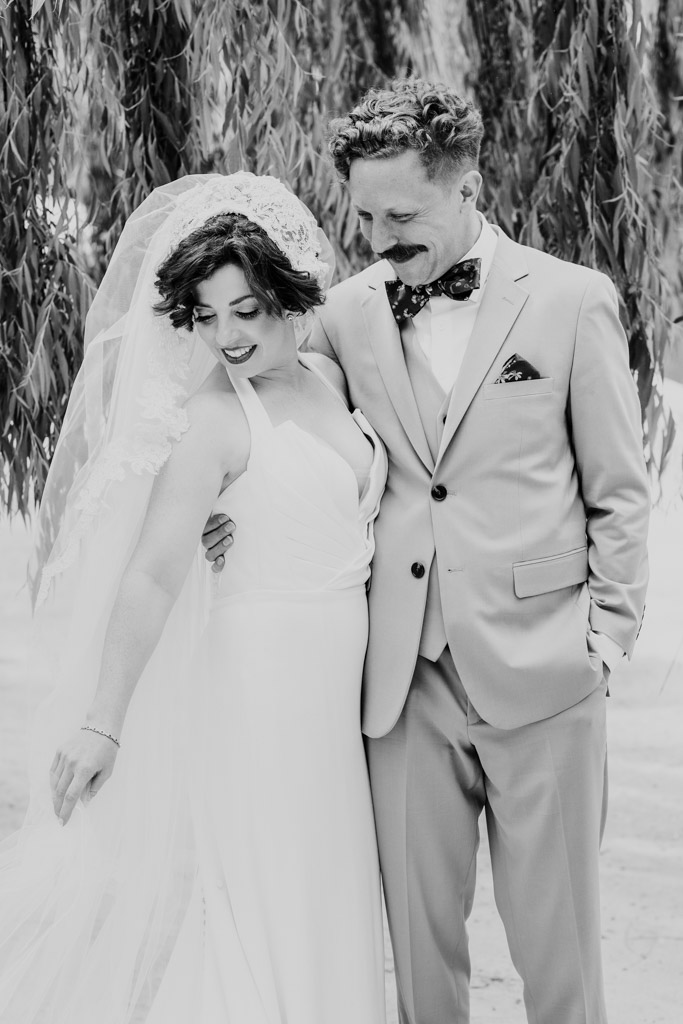 Black and white portrait of bride and groom smiling and embracing under hanging branches at Terra Mia Vineyard
