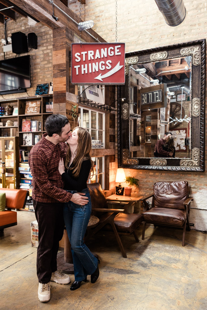 Engaged couple kisses in a cozy, rustic room under a 